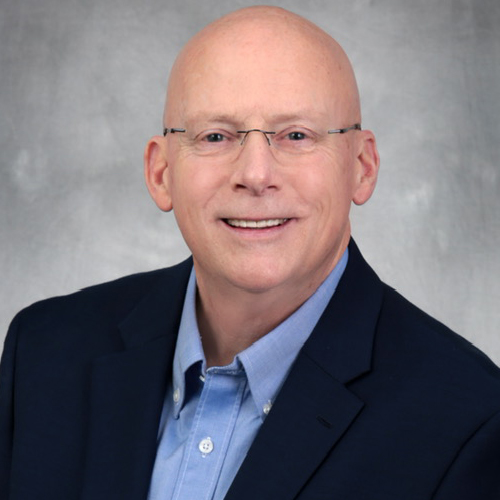 A man in a suit and glasses is smiling.