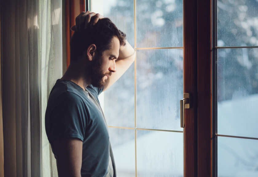 A man standing in front of a window with his hand on his head.