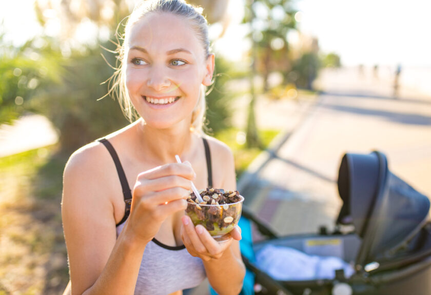 A woman eating food outside near the road.