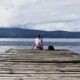 Woman sits on pier overlooking lake.