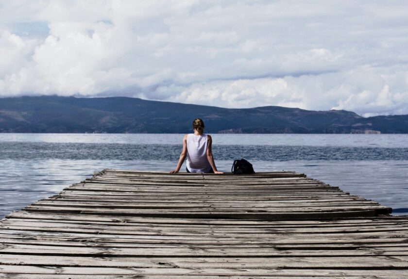 Woman sits on pier overlooking lake.