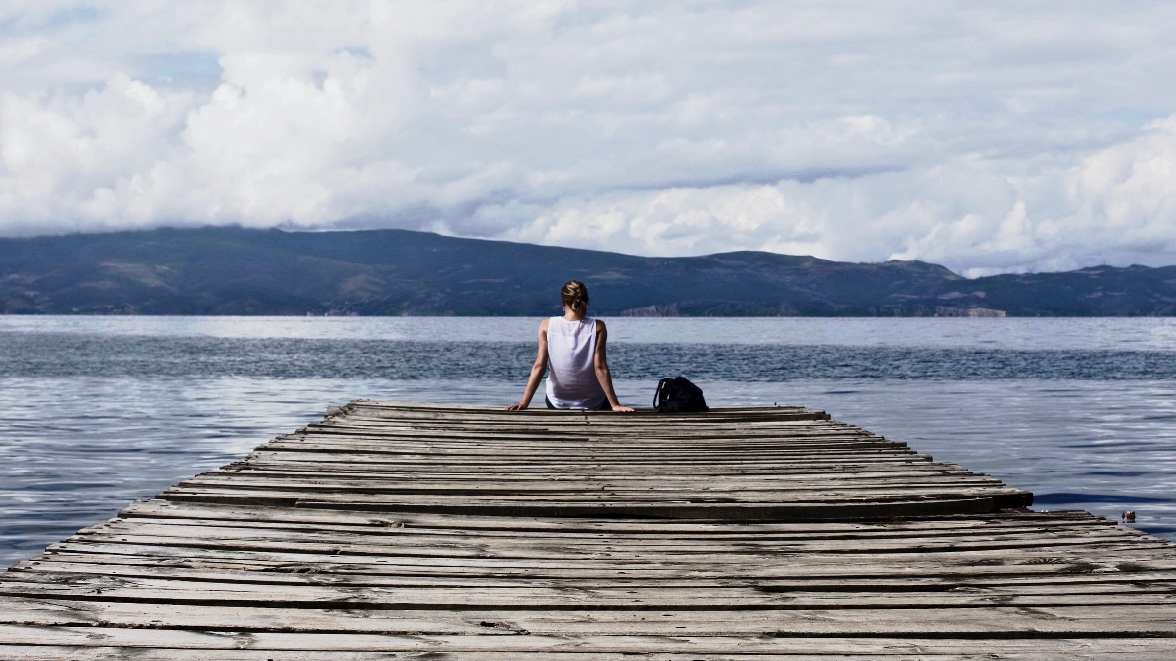 Woman sits on pier overlooking lake.