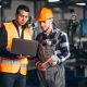 Two men in hard hats and safety vests looking at a laptop.