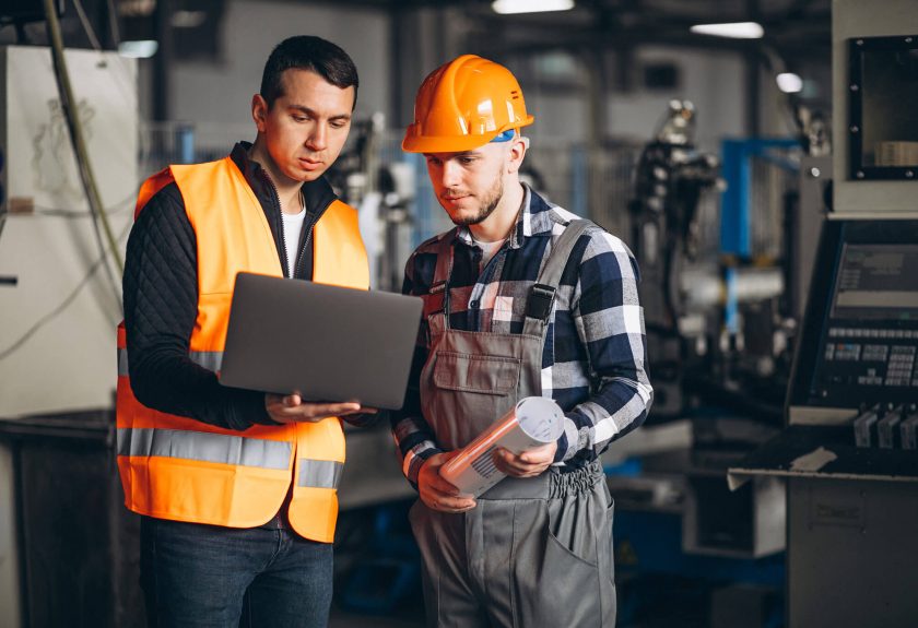 Two men in hard hats and safety vests looking at a laptop.